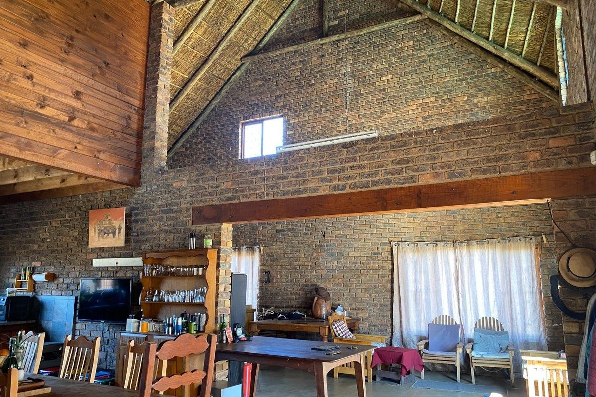 Spacious open-plan living area featuring rustic exposed brick walls, high vaulted thatched ceilings with timber beams, and durable concrete flooring.