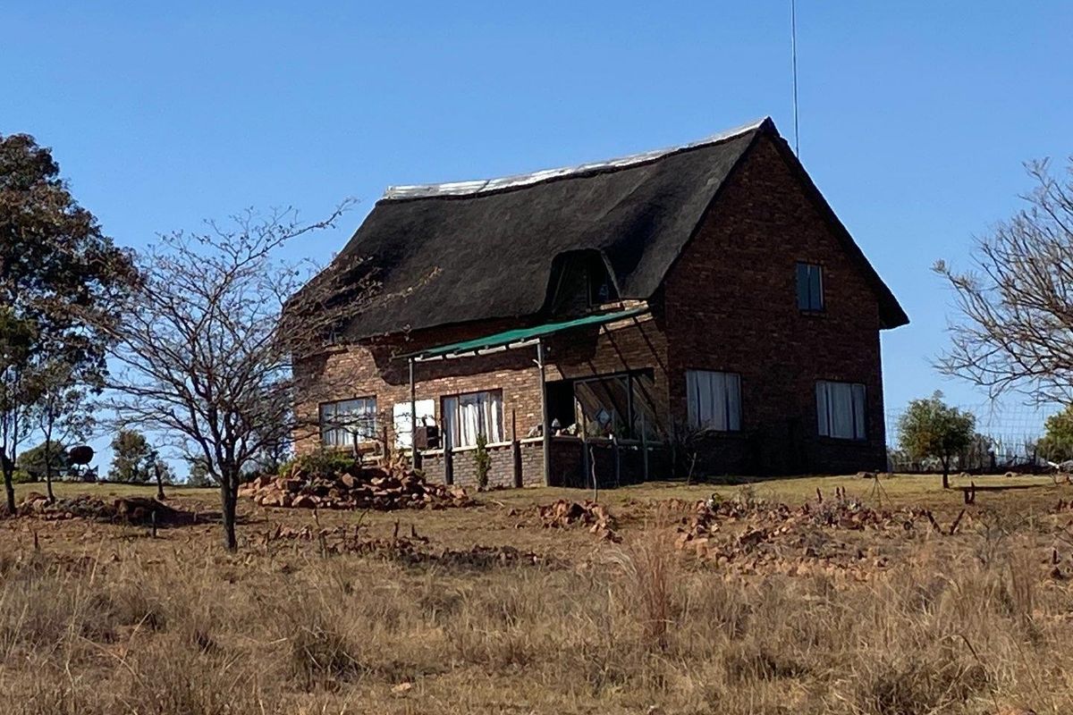 A rustic farm-style house featuring a traditional thatch roof and brick exterior, situated on a large, open rural plot.