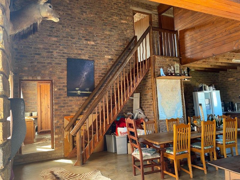 Open plan living area featuring exposed brick walls, a wooden staircase leading to a mezzanine level, and rustic timber ceiling beams.