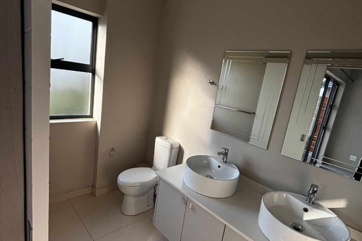 A modern, clean bathroom featuring a double vanity with vessel sinks, chrome fixtures, and neutral floor tiles.