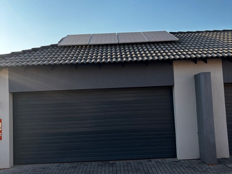 Front view of the townhouse featuring a paved driveway, automated garage door, and roof-mounted solar panels.