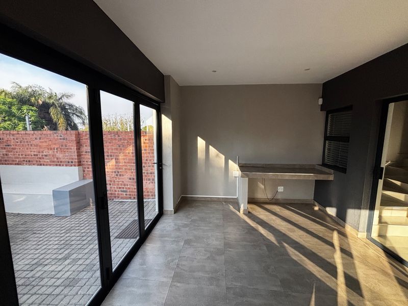 A modern, covered patio area featuring large sliding glass doors, tiled flooring, and a built-in concrete counter, offering seamless indoor-outdoor flow.