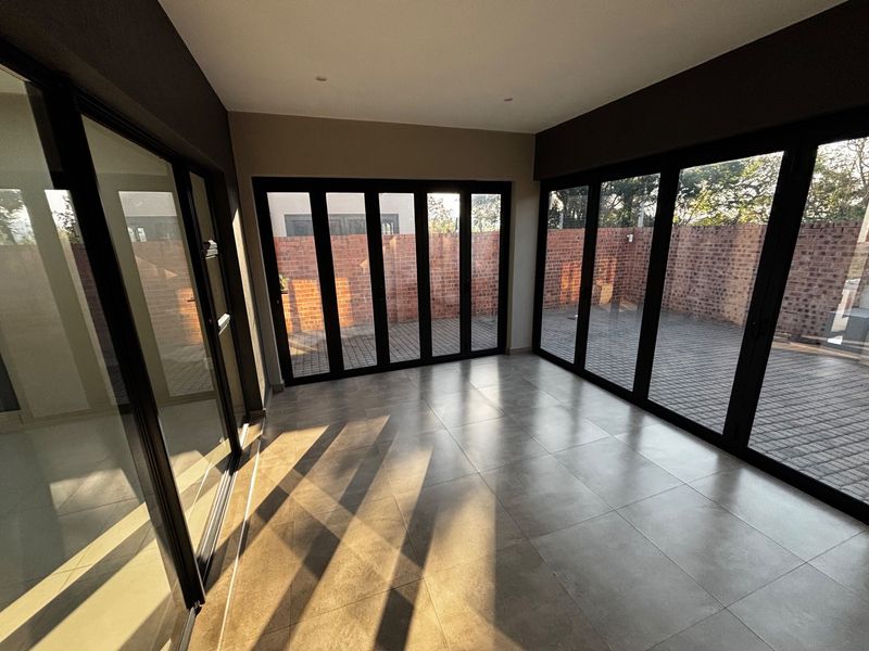 A bright, modern living area featuring large format floor tiles and expansive black aluminium stacker doors that open onto a paved rear courtyard.