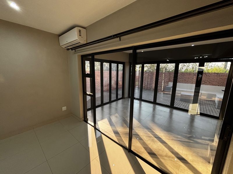 Bright and spacious living area featuring large black-framed sliding glass doors that open onto a paved patio, complete with a wall-mounted air conditioning unit.
