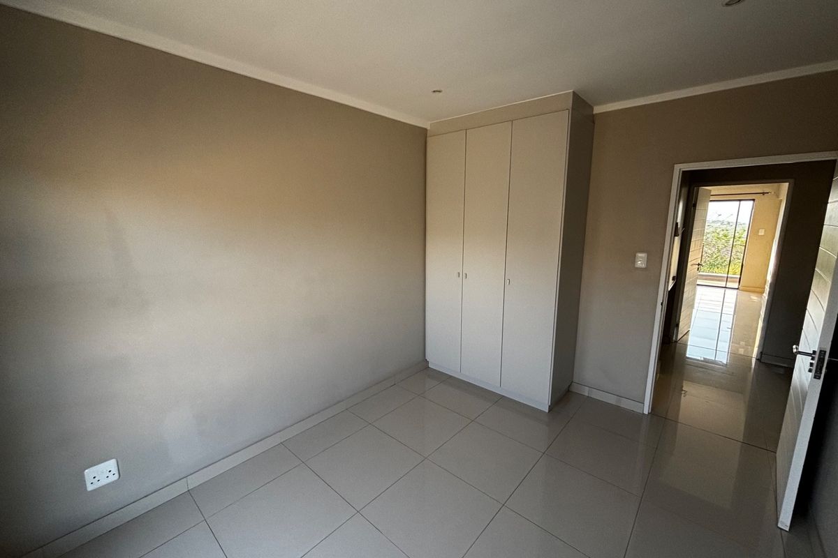 A clean, empty bedroom featuring neutral tiled flooring, built-in cupboards, and recessed lighting, offering a blank canvas for personalization.