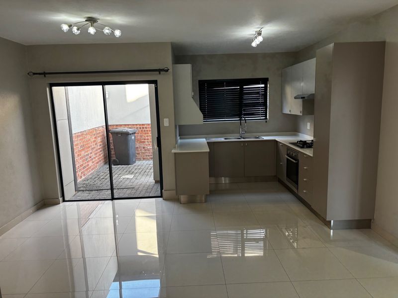 Modern open-plan kitchen featuring sleek cabinetry, built-in appliances, and tiled flooring, with direct access to a private paved courtyard through sliding glass doors.
