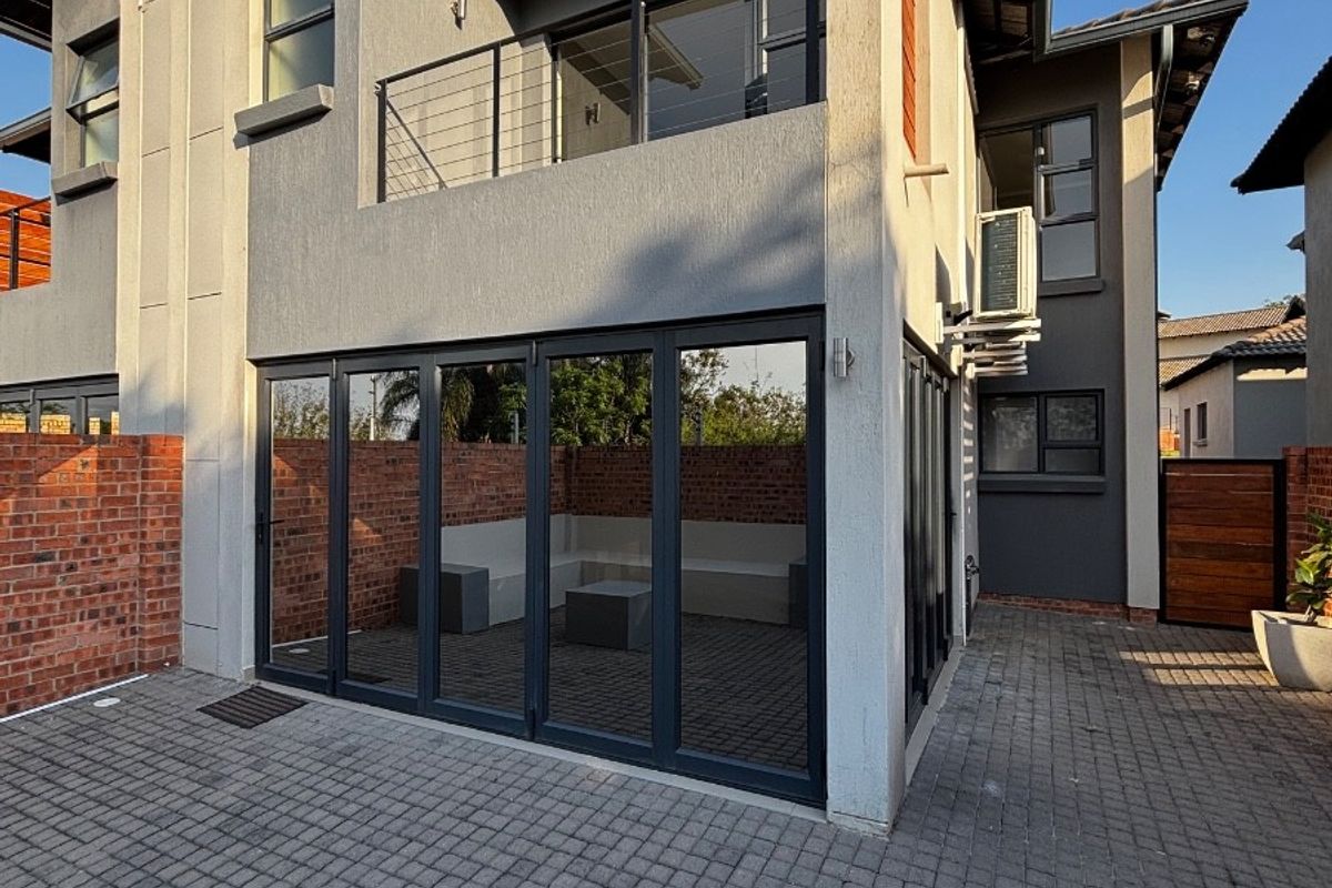 Rear view of the townhouse featuring a paved courtyard, brick boundary walls, large folding glass doors, and an upper-level balcony.