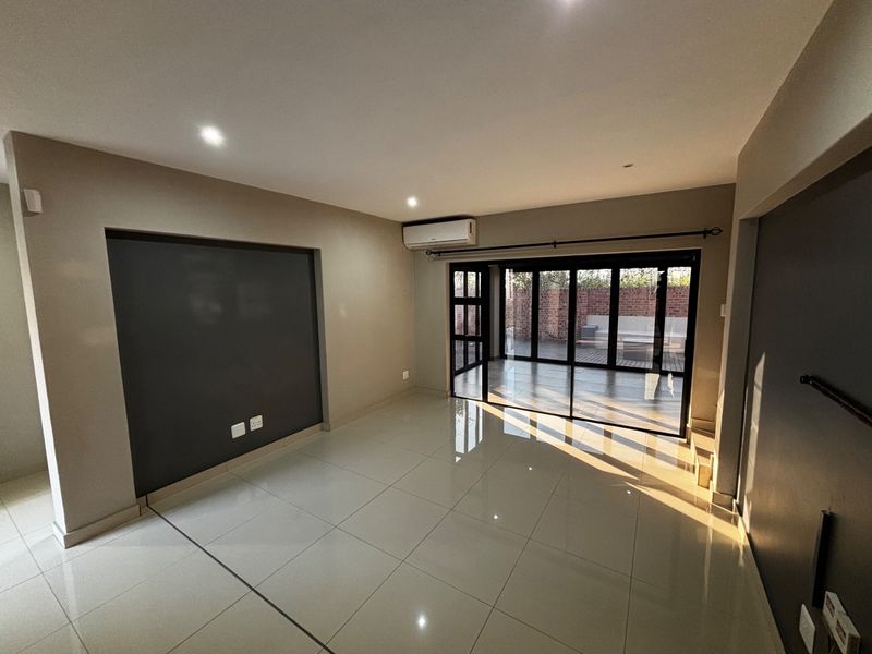 Spacious, modern living area featuring large format floor tiles, a feature wall, and sliding glass doors providing seamless access to the outdoor patio.