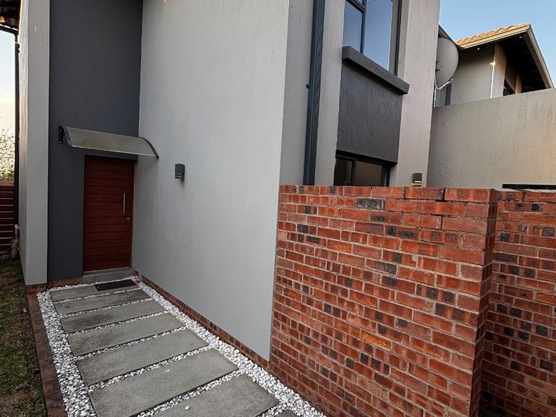 Front entrance of the townhouse featuring a modern facade, brick boundary wall, and a concrete paver walkway with decorative pebble borders.