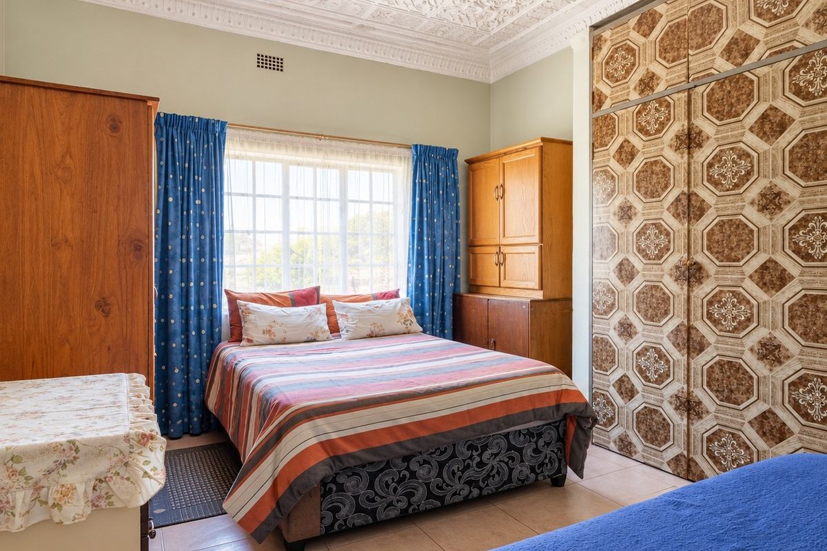 A bedroom featuring built-in cupboards, ornate ceiling detailing, and tiled flooring, offering a functional space with potential for modern updates.