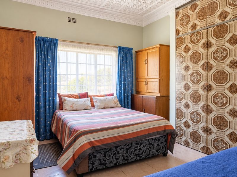 A bedroom featuring built-in cupboards, ornate ceiling detailing, and tiled flooring, offering a functional space with potential for modern updates.
