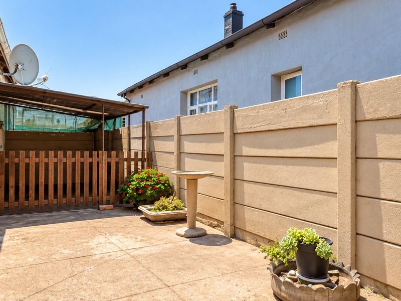 A rear exterior area featuring a paved patio, concrete boundary wall, and a covered lean-to structure, providing a functional outdoor space.
