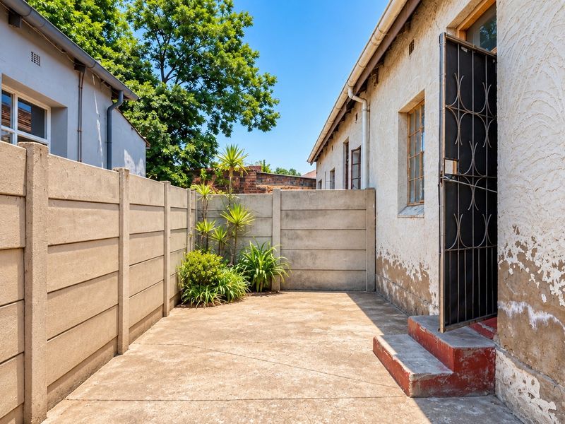 A private rear courtyard area featuring a concrete patio, enclosed by precast concrete walls, with direct access to the home via a security gate.