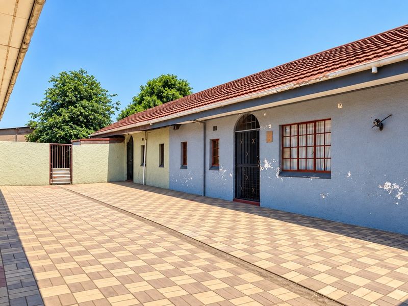 A spacious paved rear courtyard area featuring a tiled roof and exterior access points, showing signs of weathered paint and plaster.
