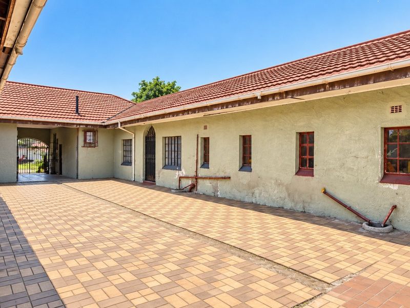 A spacious rear courtyard featuring paved flooring, tiled roofing, and exterior wall access with security bars on windows.