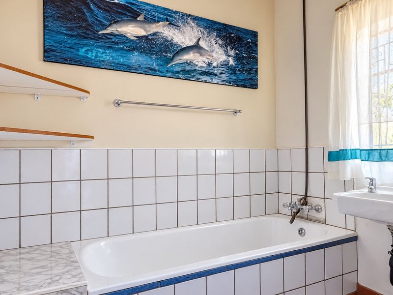 A functional bathroom featuring a built-in bathtub, wall-mounted basin, and tiled splashbacks, offering a clean space ready for modern updates.