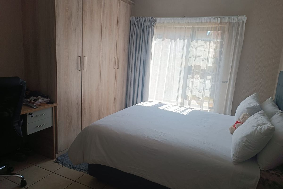 A well-lit bedroom featuring built-in wooden wardrobes, tiled flooring, and a sliding door providing access to natural light.