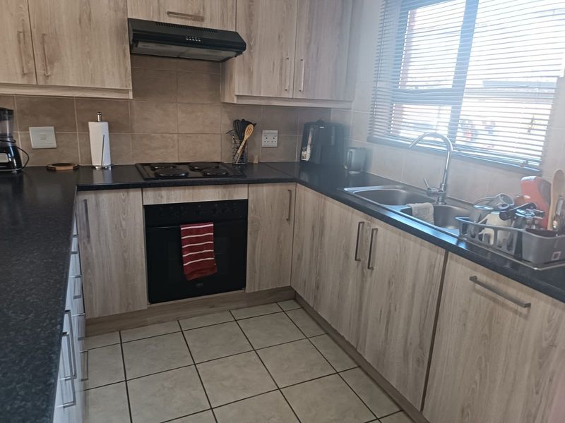 A functional kitchen featuring light wood-grain cabinetry, black granite countertops, built-in oven, electric hob, and a stainless steel double sink with tiled flooring.