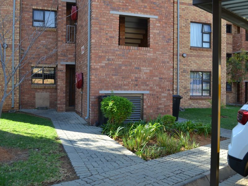 Exterior view of a face brick apartment building featuring a paved walkway, landscaped garden beds, and secure window fittings.