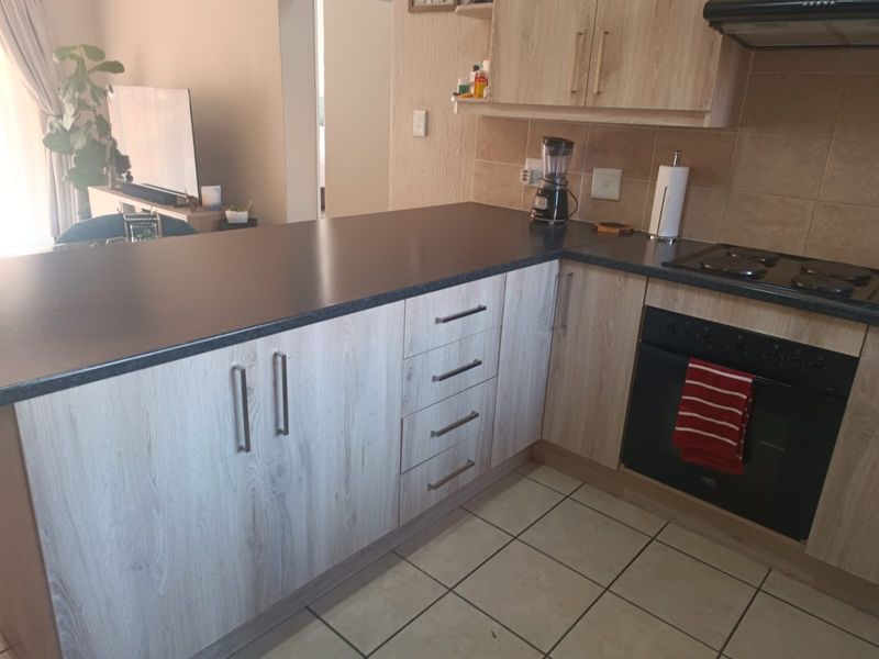 A functional kitchen featuring light wood-look cabinetry, dark countertops, built-in oven, electric hob, and tiled flooring, offering a practical layout for daily use.