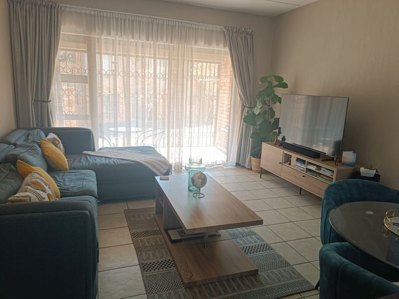 A comfortable living room featuring tiled flooring and a large sliding glass door with security gate, providing access to the outdoor area.