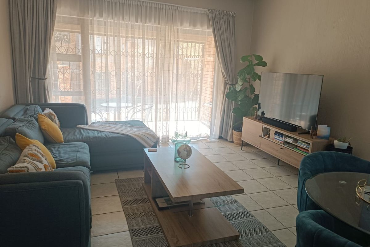 A comfortable living room featuring tiled flooring and a large sliding glass door with security gate, providing access to the outdoor area.