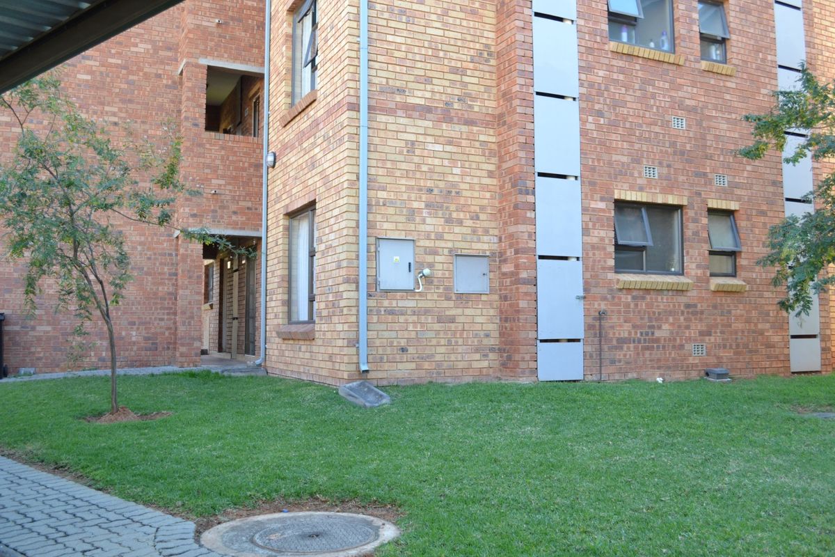 A view of the rear face brick apartment building facade featuring casement windows, a paved walkway, and a small lawn area.