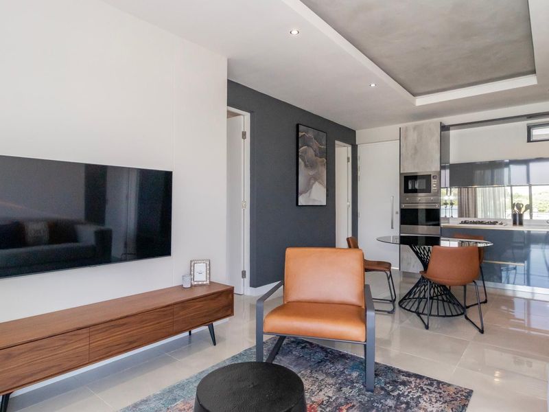 Modern open-plan living area featuring a sleek kitchen with built-in appliances, recessed ceiling lighting, and polished tiled flooring throughout.
