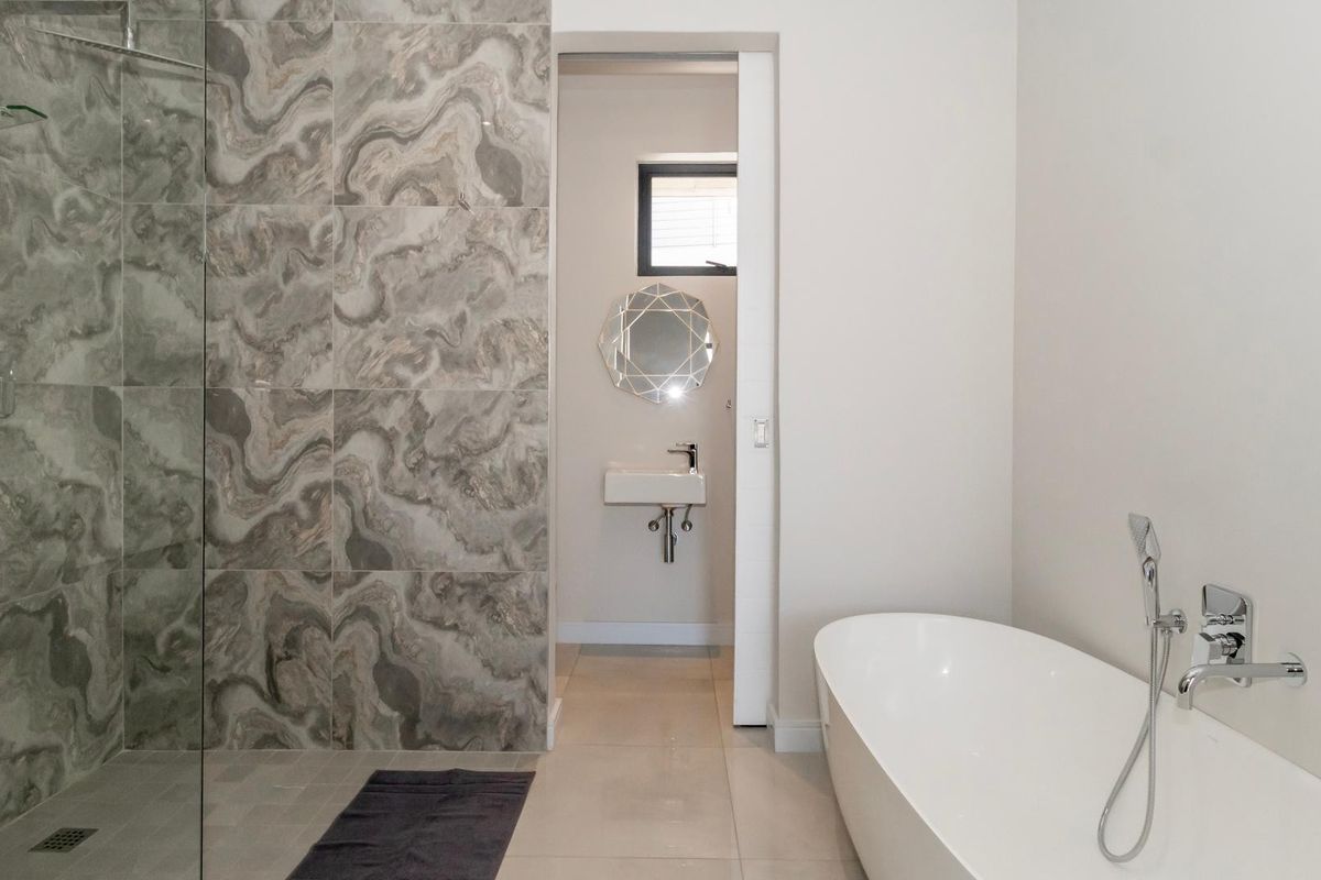 Modern bathroom featuring a sleek freestanding bathtub, a spacious walk-in shower with decorative feature tiling, and a minimalist wall-mounted basin.