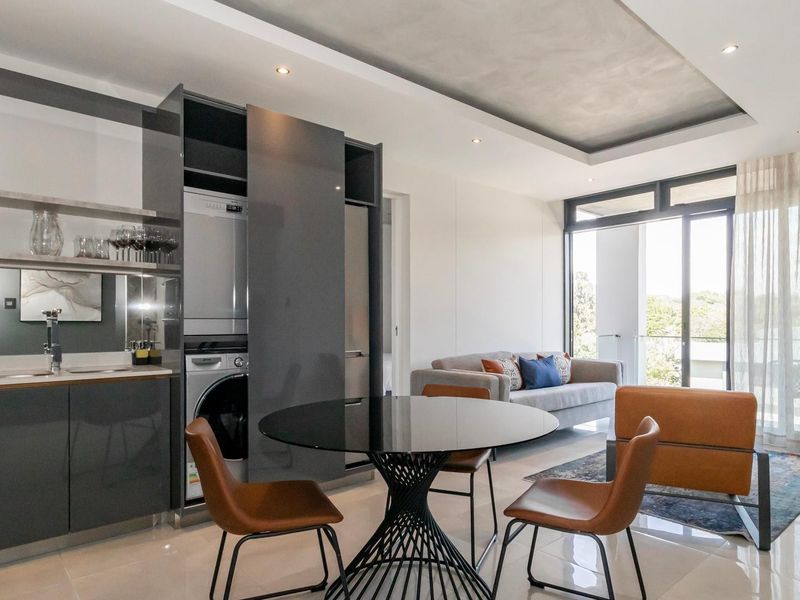 Modern open-plan living area featuring a sleek kitchen with integrated laundry, recessed ceiling lighting, and large sliding doors leading to a balcony.