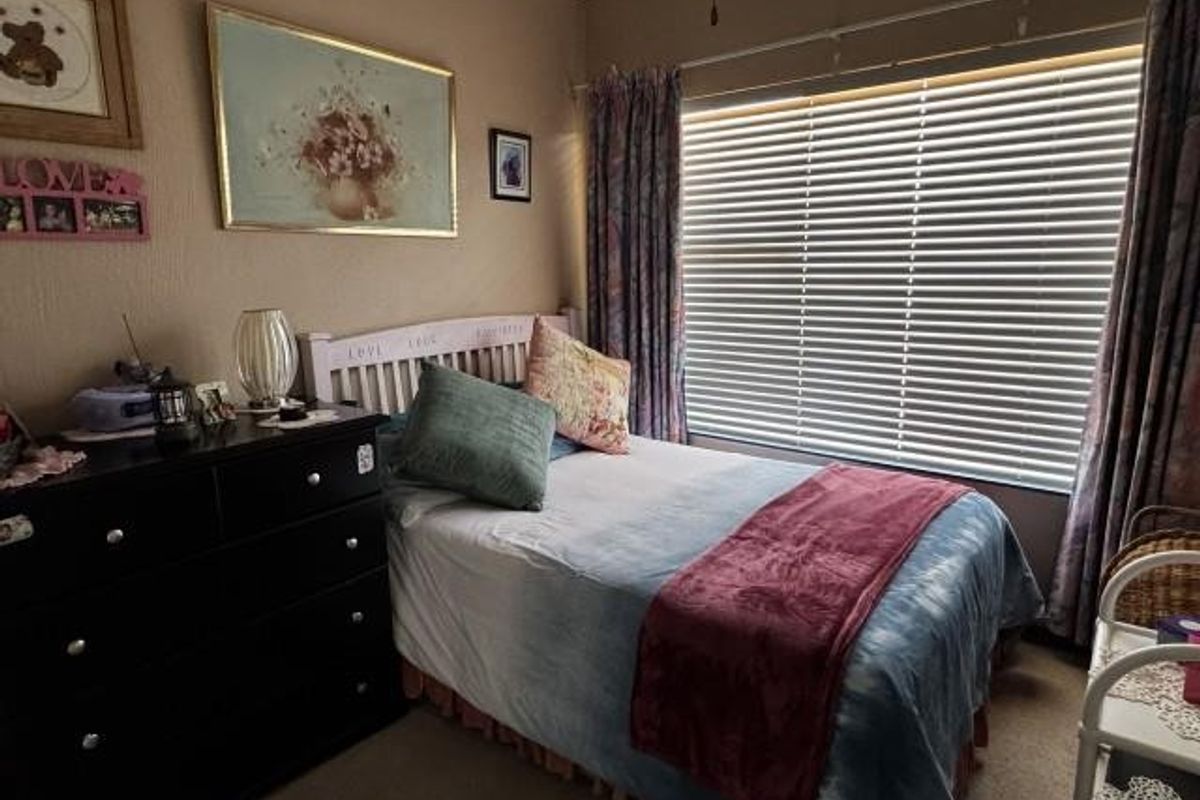 A cozy bedroom featuring carpeted flooring, a large window with venetian blinds, and neutral wall finishes.
