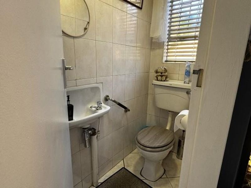 A compact guest bathroom featuring tiled walls, a wall-mounted basin with a grab rail, and a standard toilet.
