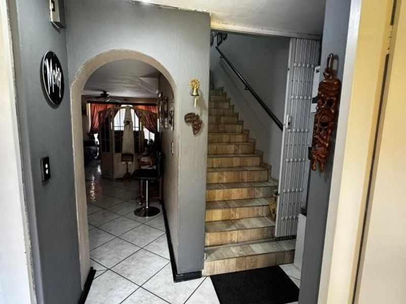 Entryway featuring tiled flooring, an arched transition to the living area, and a staircase with a metal handrail and security gate.