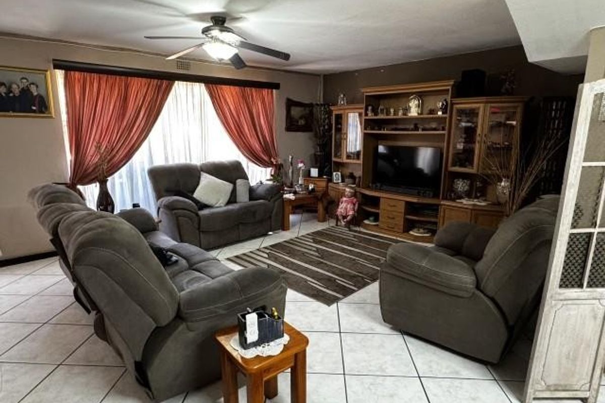 A spacious living room featuring tiled flooring, a ceiling fan, and built-in wooden cabinetry for storage and media display.