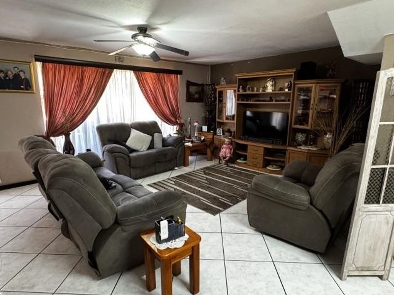 A spacious living room featuring tiled flooring, a ceiling fan, and built-in wooden cabinetry for storage and media display.