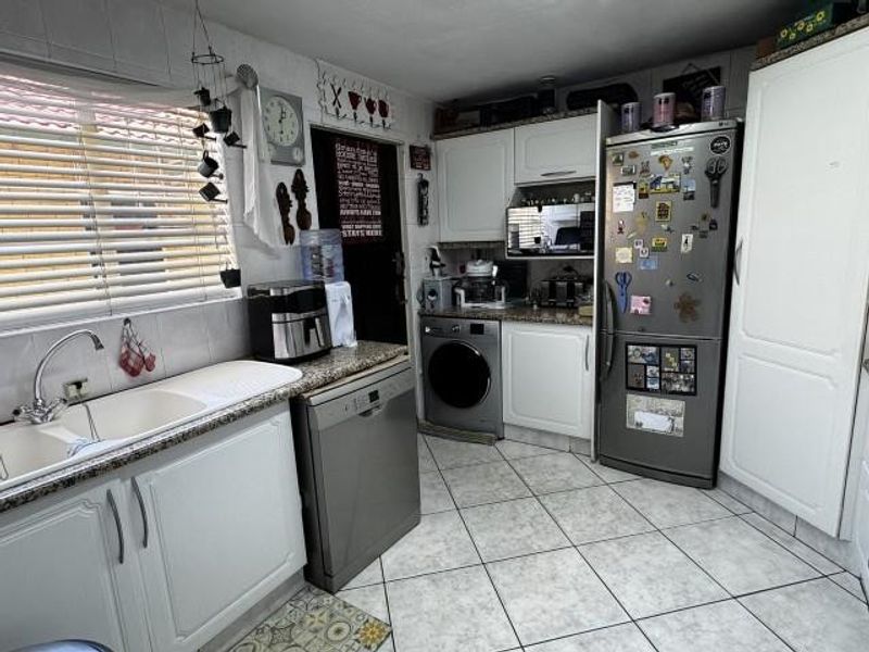 A functional kitchen featuring white cabinetry, granite countertops, a double basin sink, and tiled flooring, providing a practical workspace for daily meal preparation.