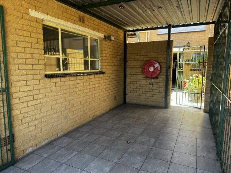 A covered outdoor patio area featuring tiled flooring, brick walls, and a corrugated metal roof, equipped with a wall-mounted fire hose reel.