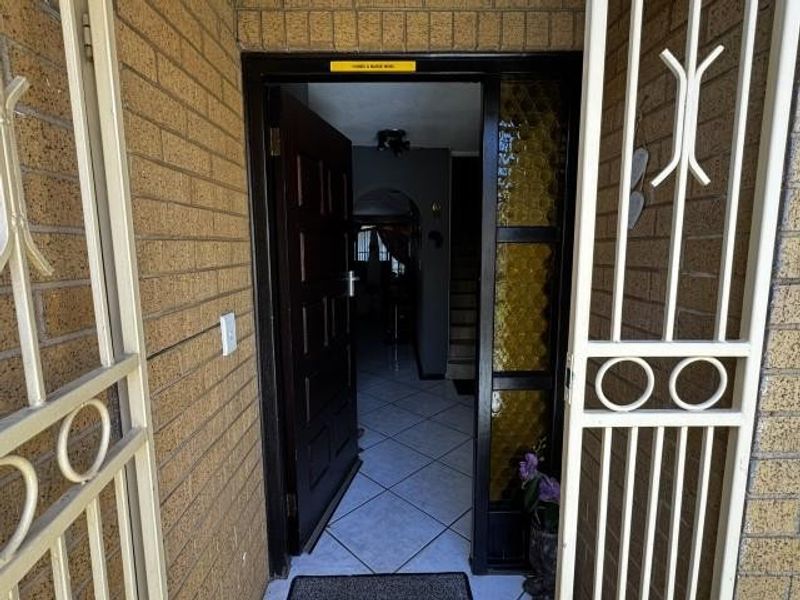 Entrance area featuring a security gate, brick exterior wall, and a timber front door leading into a tiled interior hallway.