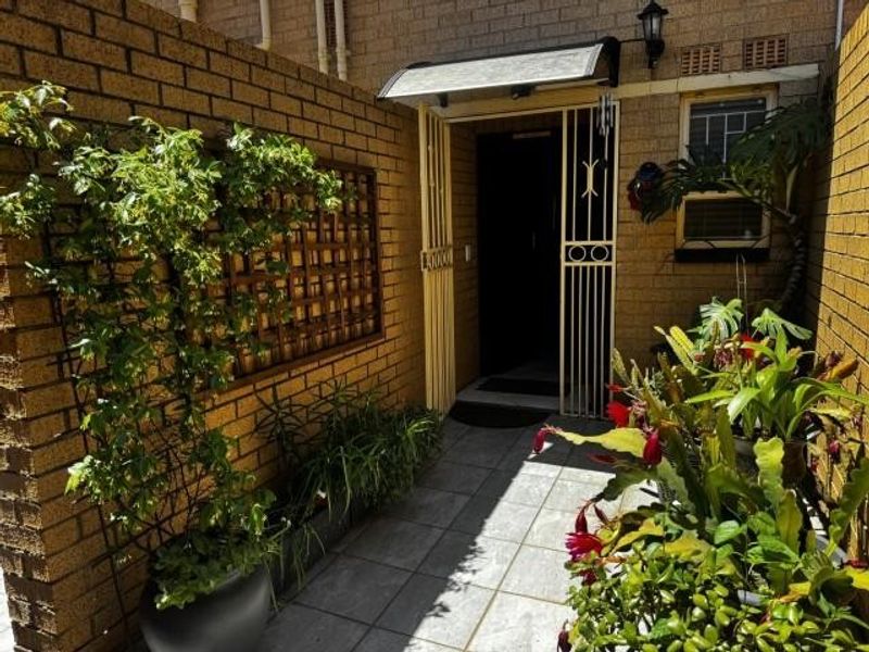 A private entrance area featuring brick walls, tiled flooring, a security gate, and a protective awning over the doorway.