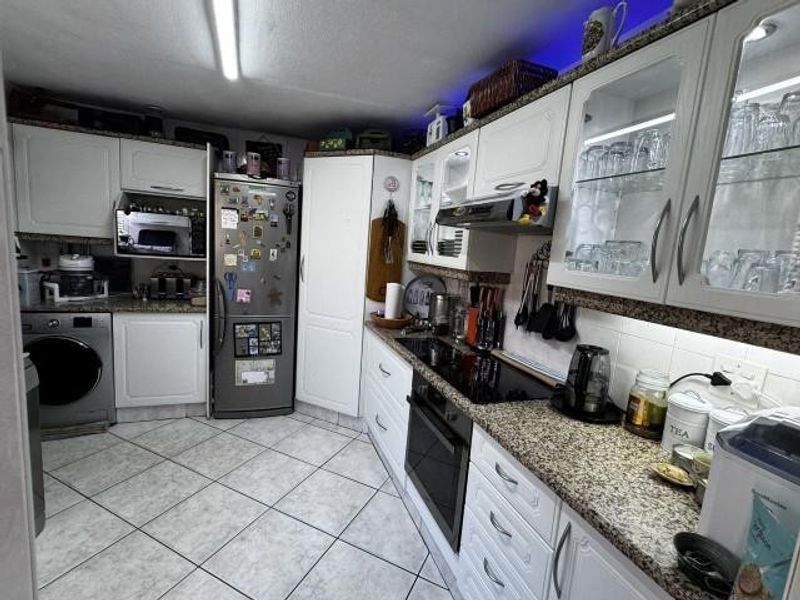 A functional kitchen featuring white cabinetry, granite countertops, built-in appliances, and tiled flooring with integrated lighting.