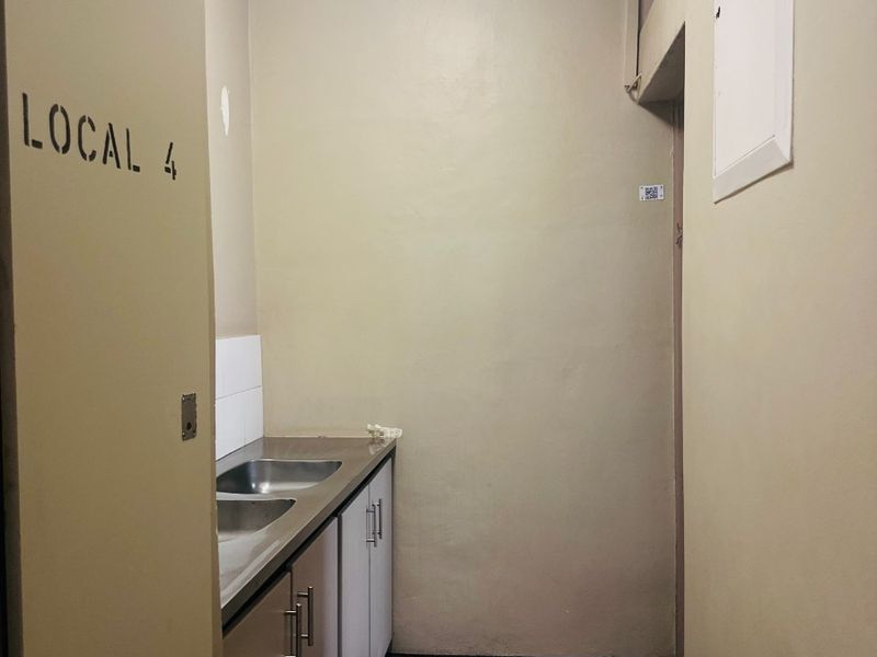 A compact office kitchenette featuring built-in cabinetry, a stainless steel sink, and tiled flooring.
