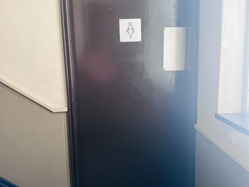 A hallway area featuring a dark-painted door with signage and an adjacent staircase, showing signs of wear on the surrounding wall finishes.