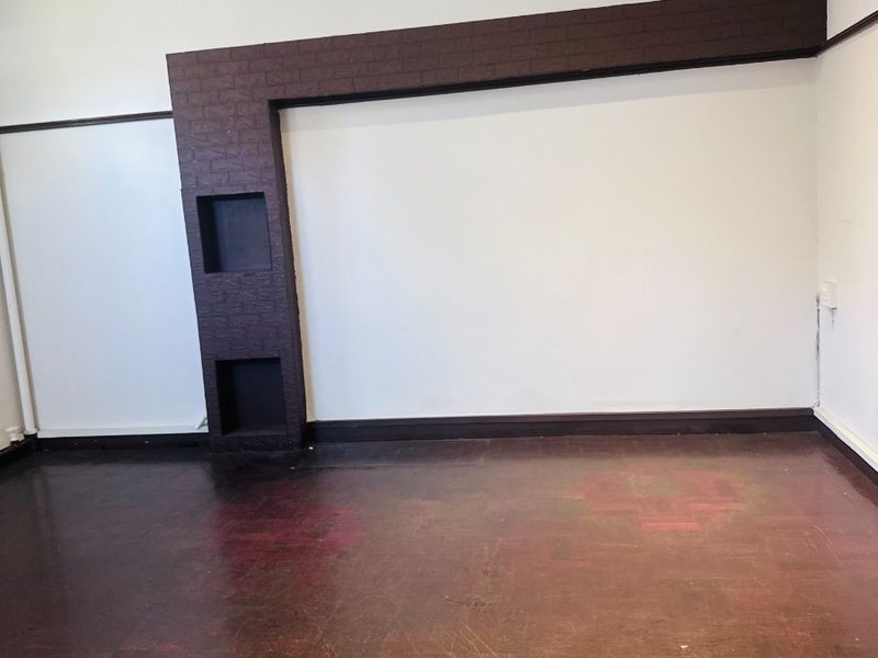 An empty office space featuring a unique dark brick feature wall with built-in niches, recessed ceiling lighting, and traditional parquet flooring.