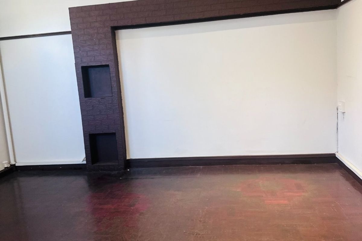 An empty office space featuring a unique dark brick feature wall with built-in niches, recessed ceiling lighting, and traditional parquet flooring.