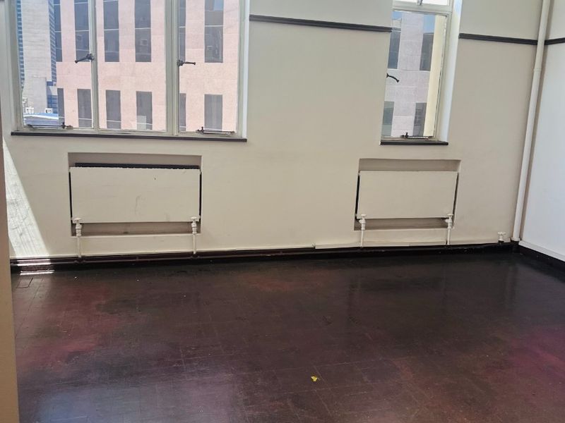 Empty office space featuring original parquet flooring, dual radiators, and large casement windows providing natural light and city views.