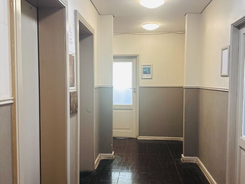 A functional office building hallway featuring elevator access, tiled flooring, and neutral wall finishes with overhead lighting.