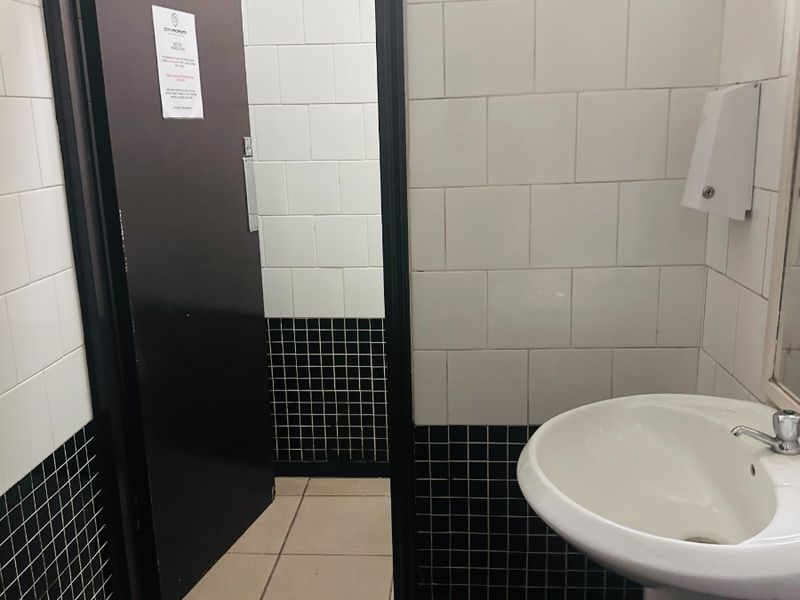A functional office bathroom featuring a pedestal basin, wall-mounted soap dispenser, and classic black and white tiled finishes.