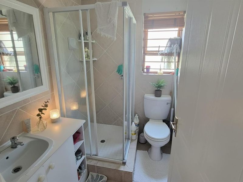 A compact bathroom featuring a shower enclosure, vanity basin, and toilet with neutral wall and floor tiling.