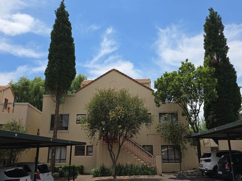 Front elevation of a multi-story townhouse complex featuring a stucco facade, tiled roof, and dedicated covered carport parking bays.