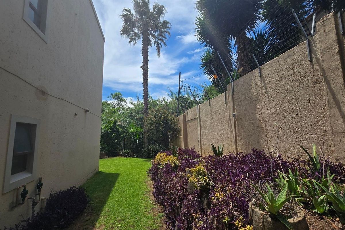 A side garden area featuring a lawn, landscaped garden beds, and a perimeter wall equipped with electric fencing.